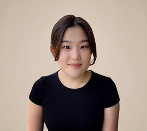 Hyeree Ellis is wearing black and smiles at the camera in front of a beige background.