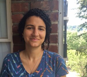 Grad Student Claire Baytaş stands outside against a brick wall and smiles at the camera.