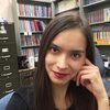 Grad student Sabrina Lee sits in an office with bookshelves behind her; she smiles at the camera