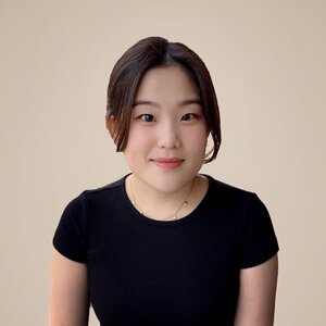 Hyeree Ellis is wearing black and smiles at the camera in front of a beige background.